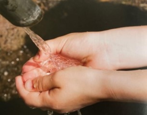 Deux mains recueillant une eau claire coulant d’un bec.